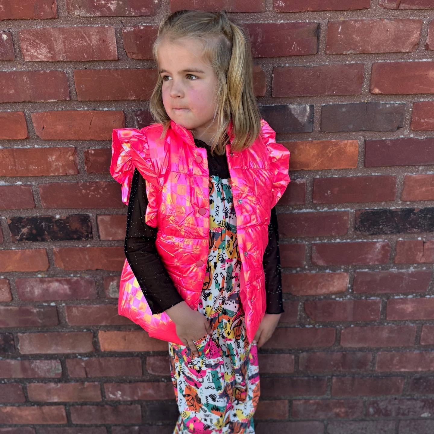 Child wearing hot pink puffer vest over a sequin lace top with 80's retro western style romper